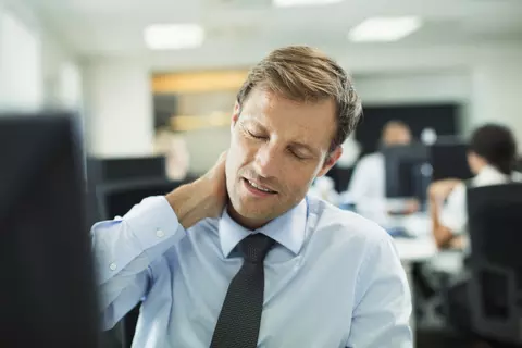 Man op kantoor die aan zijn nek voelt