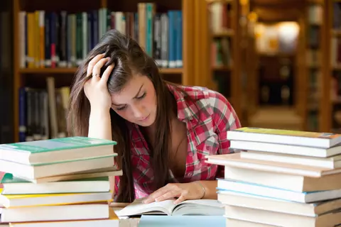 Vrouw met hand in haar haar, aan tafel met stapel boeken