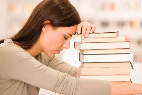 Vrouw met hoofd op stapel boeken